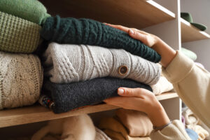 Woman taking warm sweaters from shelf in wardrobe, closeup